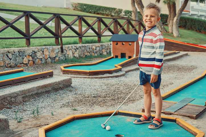 Cheerful boy playing mini golf on the territory of the hotel